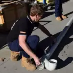 Worker assembling white PVC pipes outdoors on concrete surface in bright sunlight