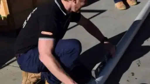 Worker assembling white PVC pipes outdoors on concrete surface in bright sunlight