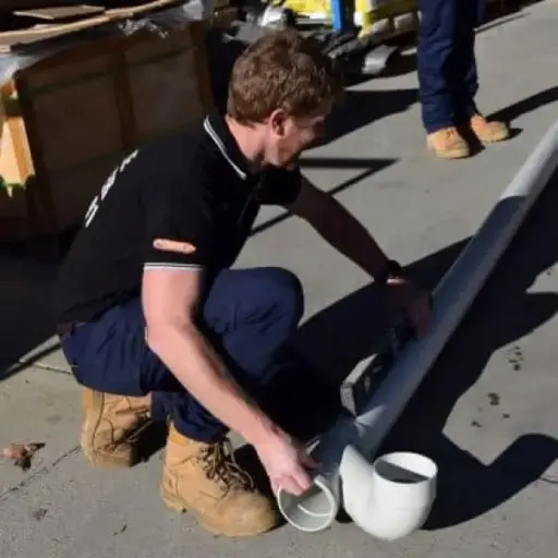Worker assembling white PVC pipes outdoors on concrete surface in bright sunlight