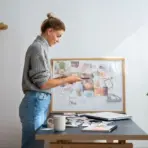 Woman reviewing paper materials at a desk with mood board and laptop in cozy workspace