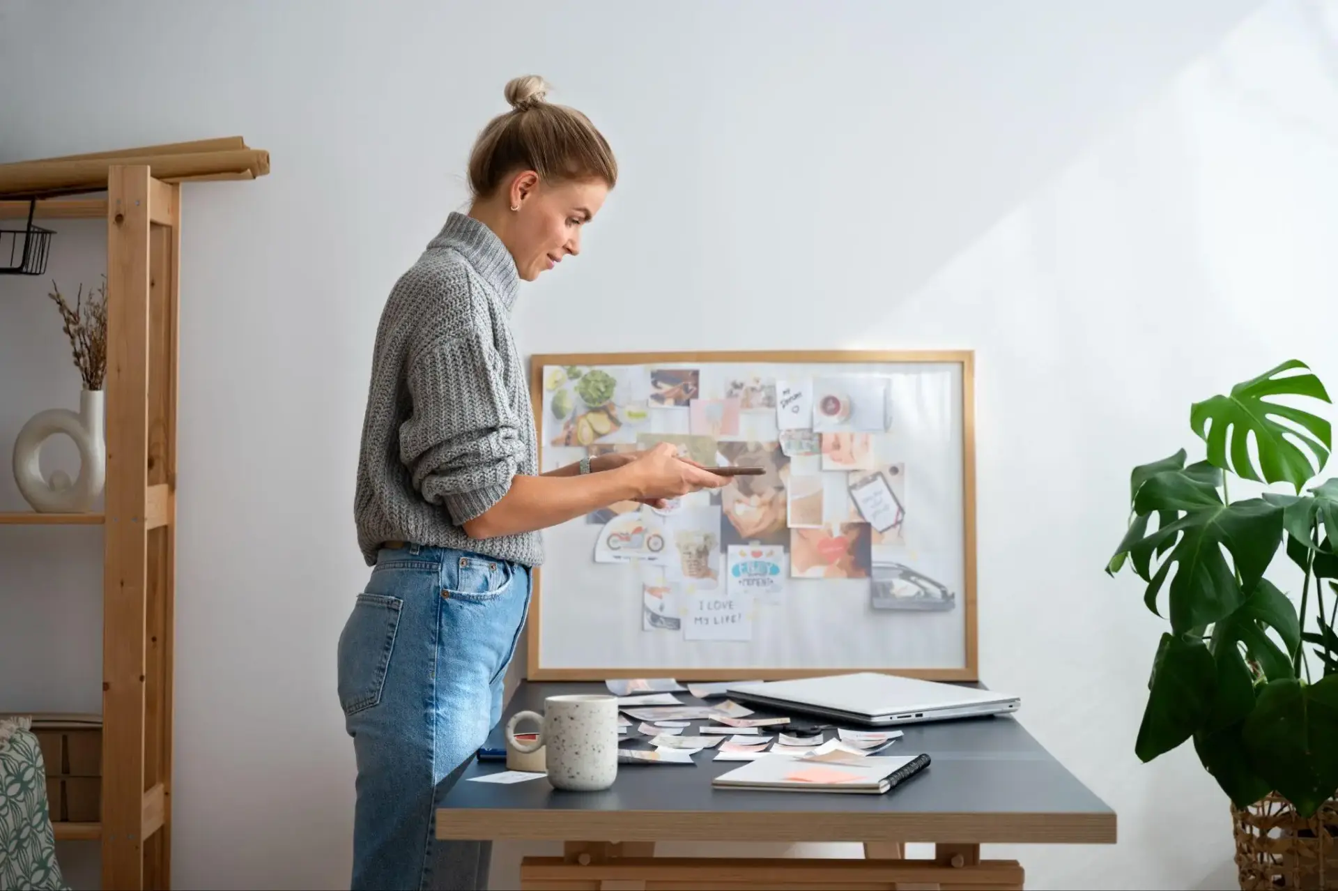 Woman reviewing paper materials at a desk with mood board and laptop in cozy workspace