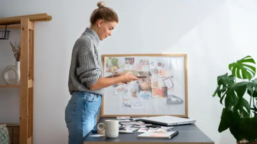 Woman reviewing paper materials at a desk with mood board and laptop in cozy workspace