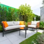 Outdoor patio with wicker furniture and orange cushions surrounded by lush greenery and trellis fencing