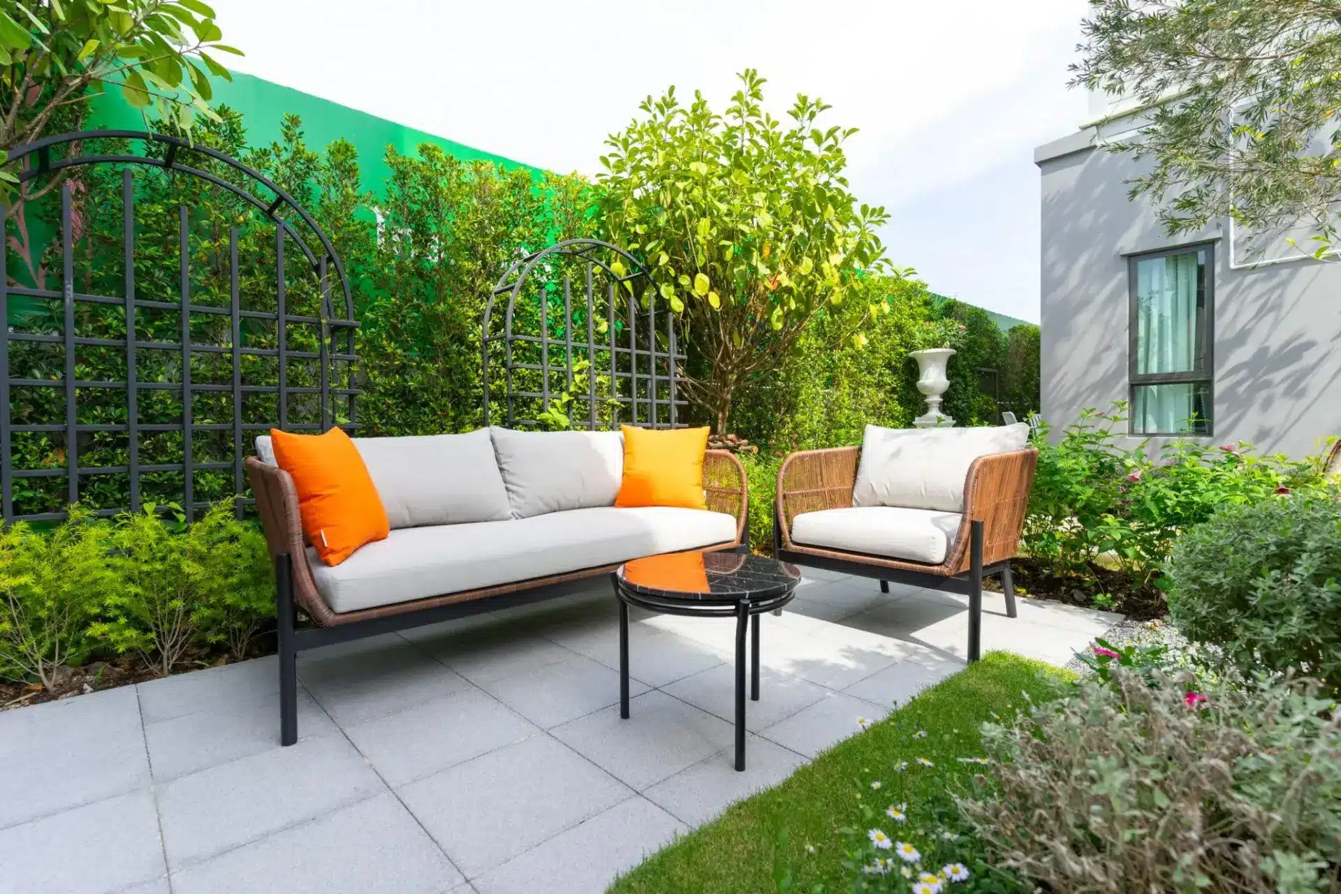 Outdoor patio with wicker furniture and orange cushions surrounded by lush greenery and trellis fencing