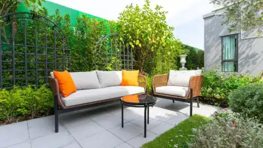 Outdoor patio with wicker furniture and orange cushions surrounded by lush greenery and trellis fencing