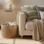 Cozy living room with textured pillows, knit throw on beige sofa, wicker basket, wooden sideboard
