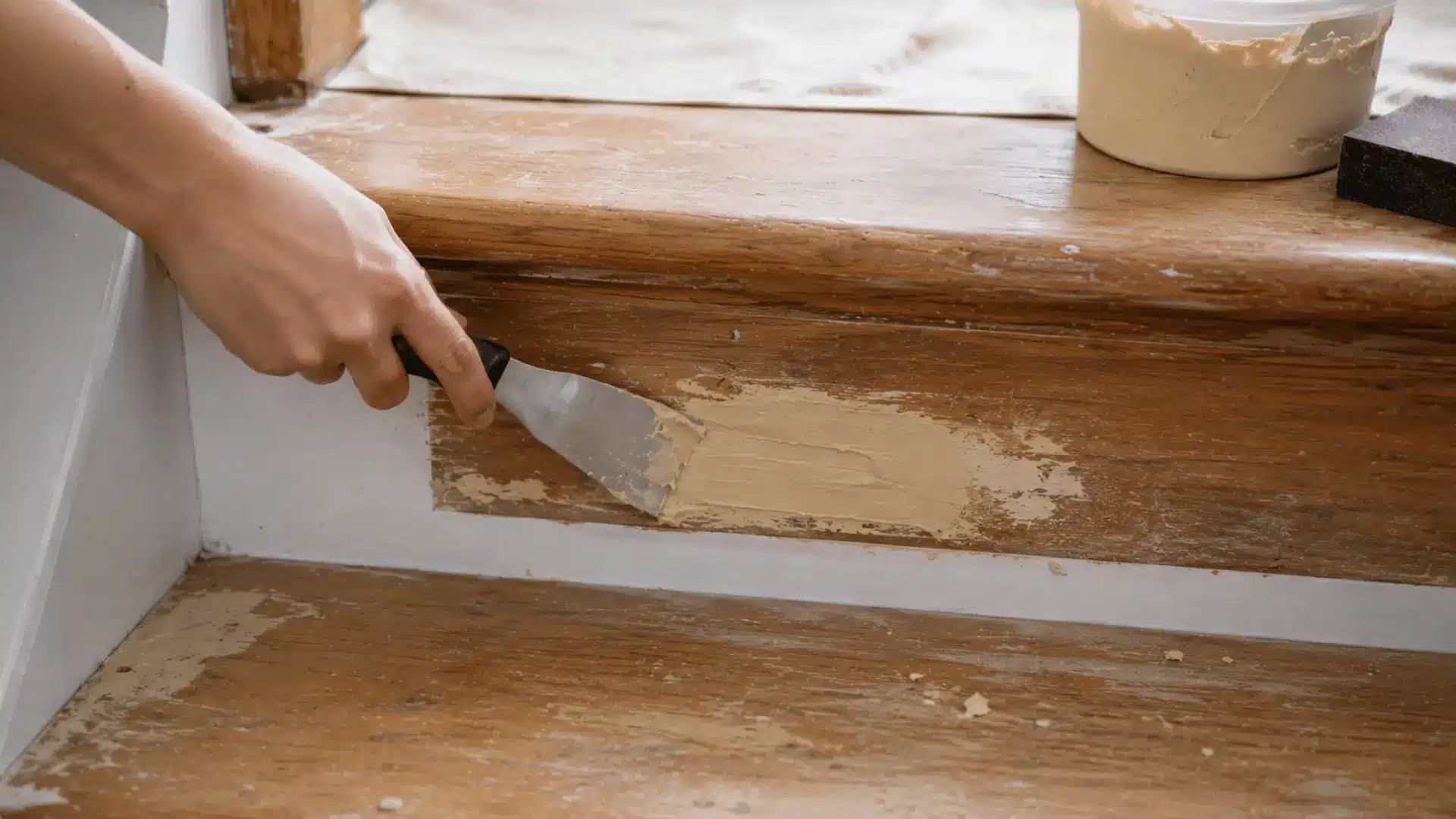 hand smoothing wood filler into cracks and nail holes on worn wooden stairs before painting