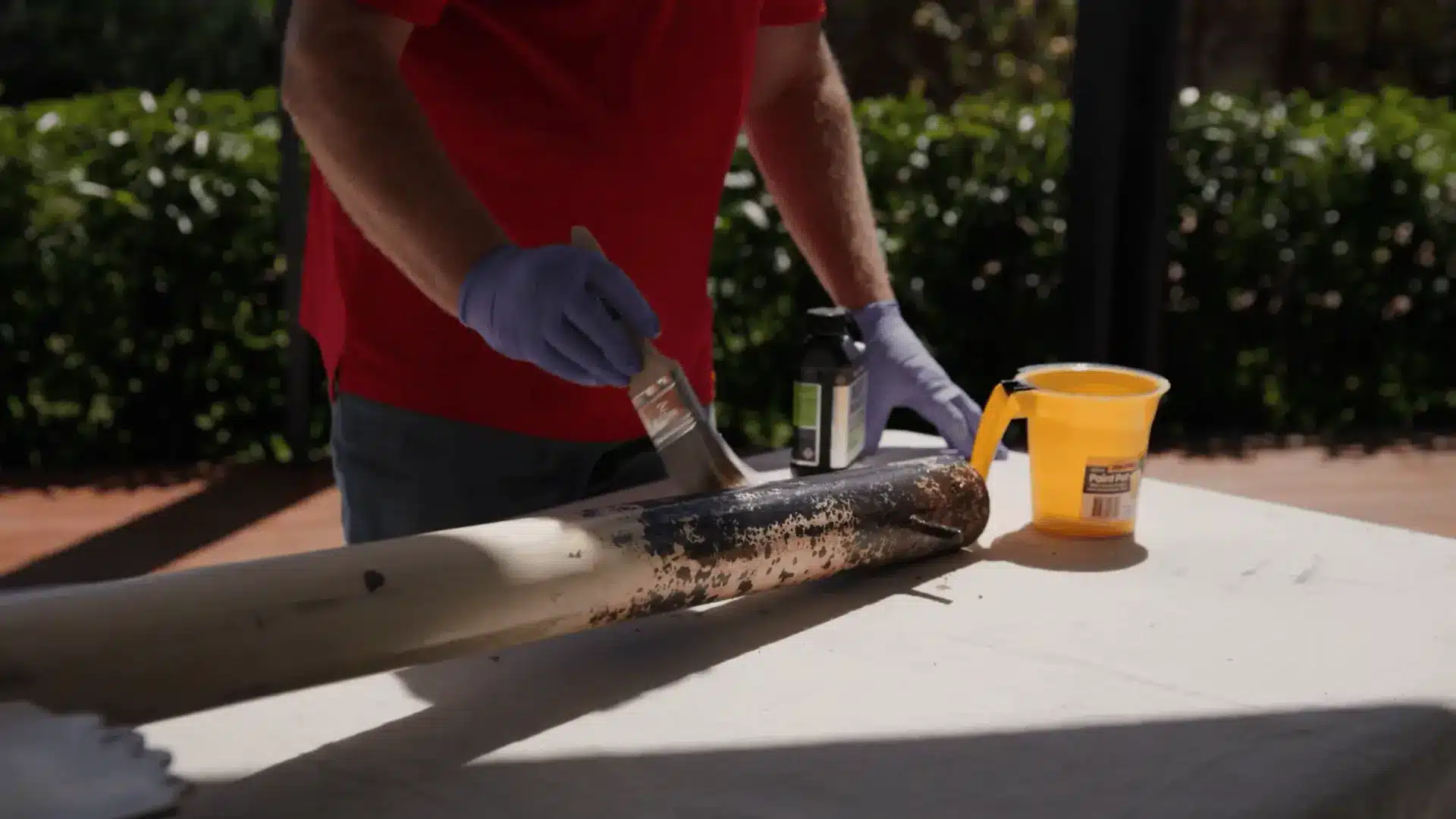 person applying metal primer with a paintbrush to a sanded metal pipe before painting for better adhesion and durability