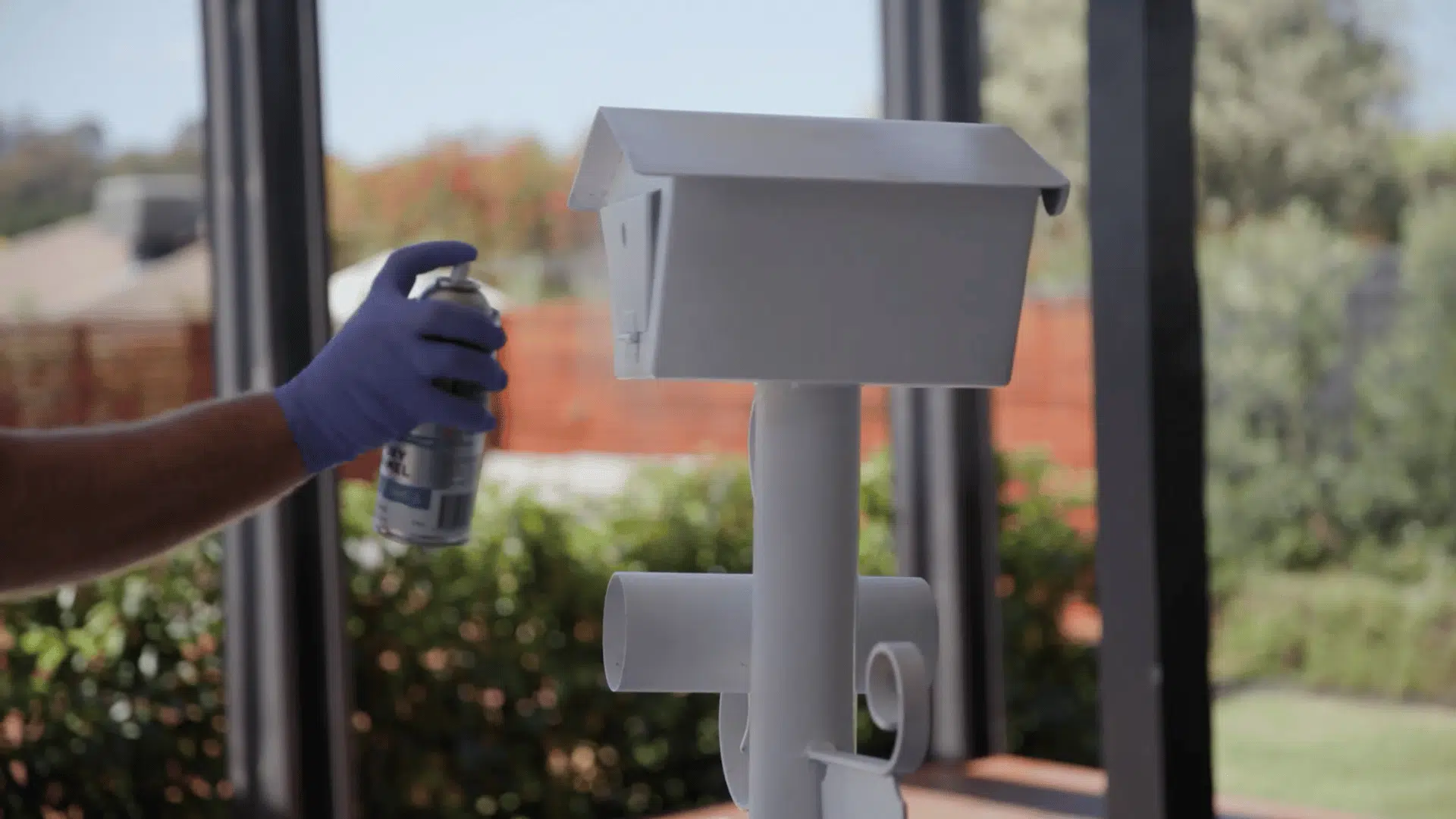 person spray painting a primed metal mailbox post with white paint for a smooth and even finish