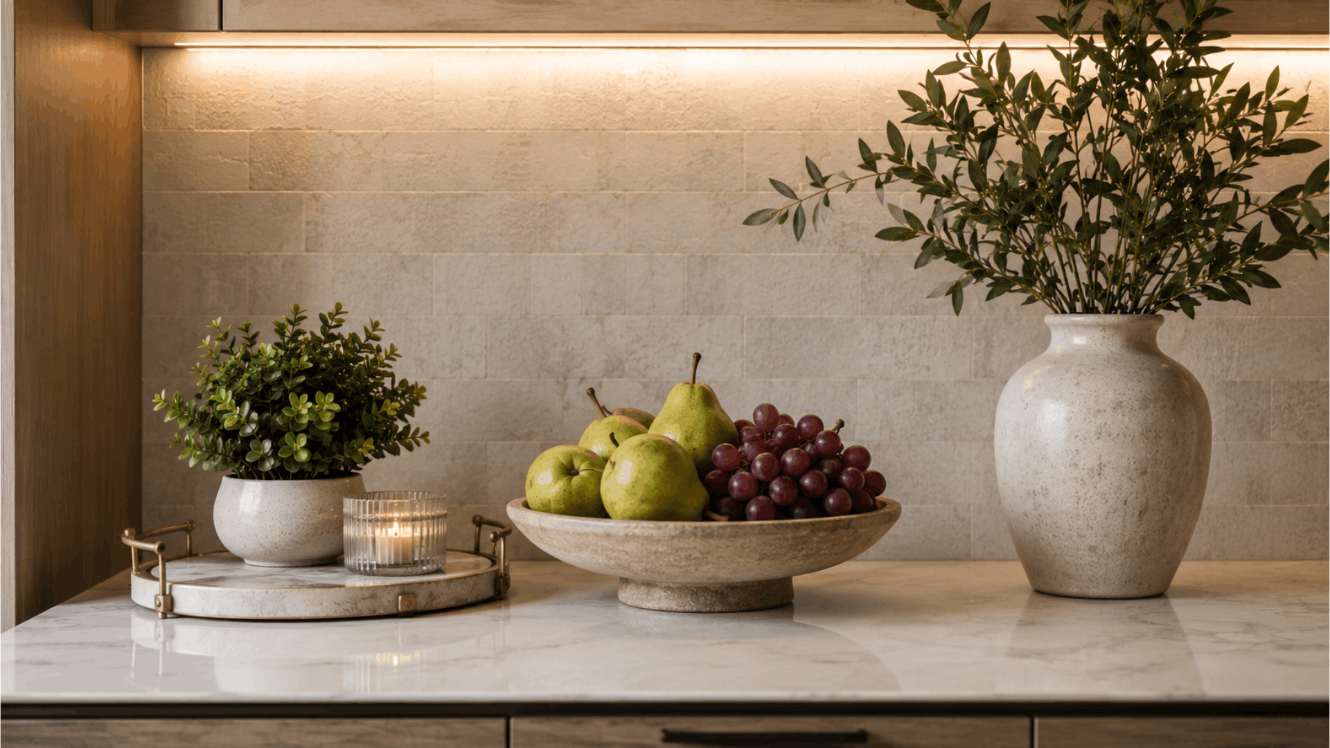 styled kitchen countertop with decorative tray plant candle fruit bowl and ceramic vase beneath warm under cabinet lighting