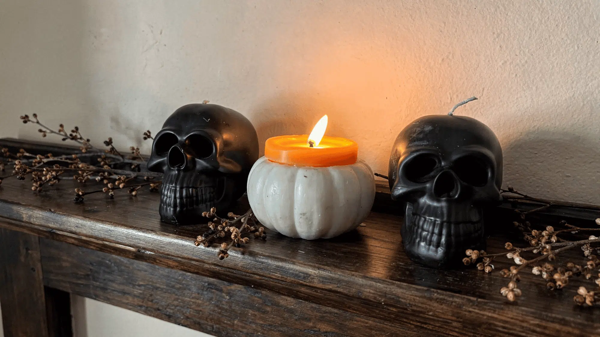 three black candles in skull and pumpkin jars on a dark wooden mantel with branches