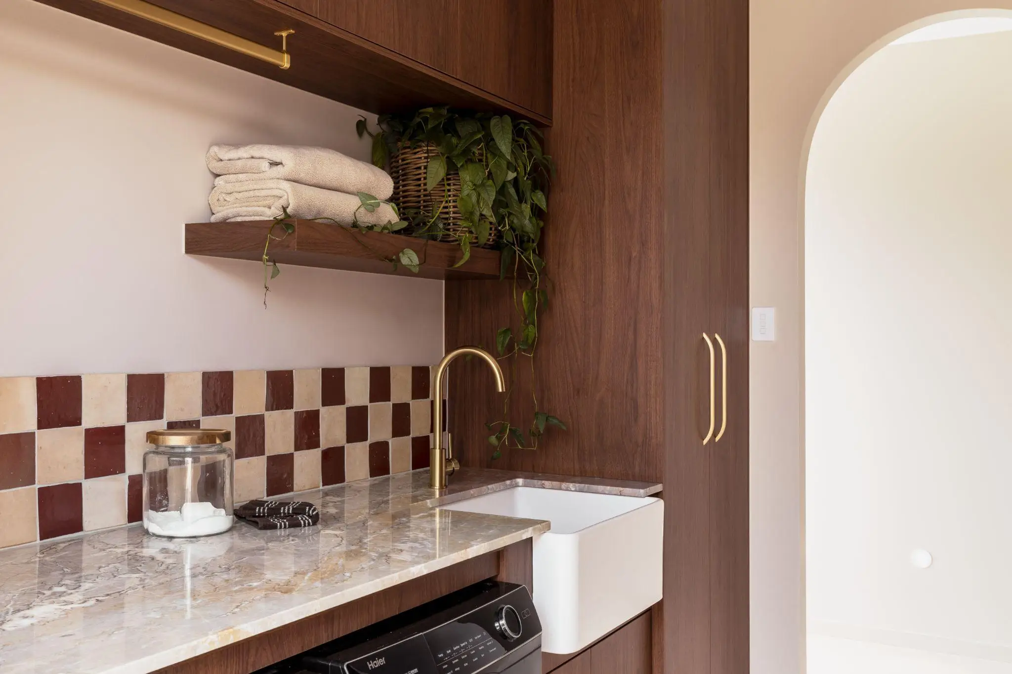 Marble countertop with farmhouse sink, wooden shelves, and potted plant in stylish laundry room
