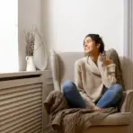 Woman in cozy sweater sitting on armchair in bright living room