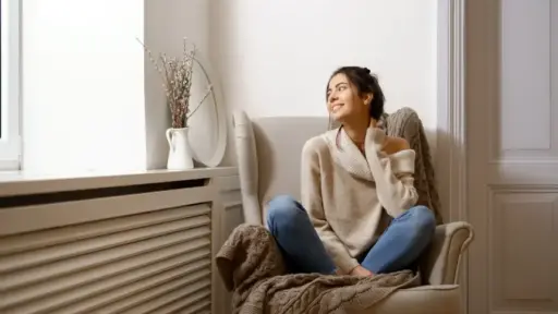 Woman in cozy sweater sitting on armchair in bright living room