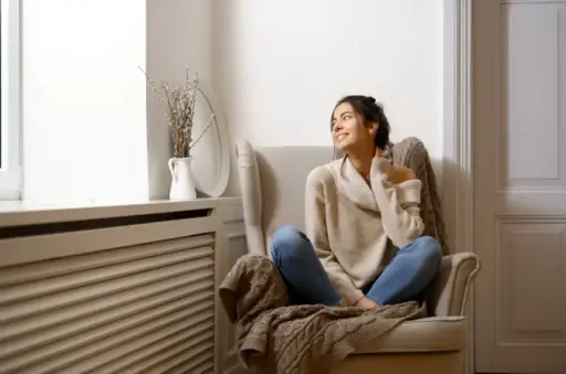 Woman in cozy sweater sitting on armchair in bright living room