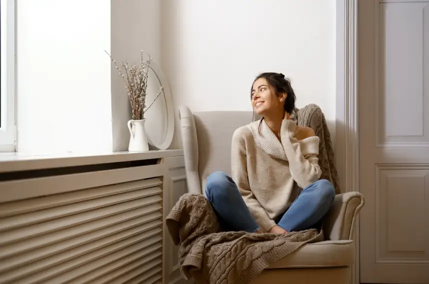 Woman in cozy sweater sitting on armchair in bright living room