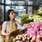 Florist in a shop arranging pink roses with clipboard in hand