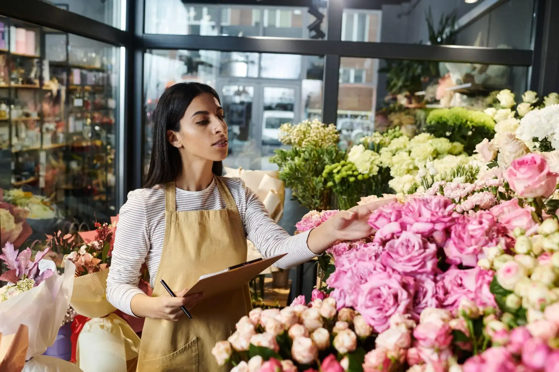Florist in a shop arranging pink roses with clipboard in hand