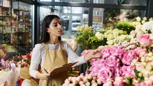 Florist in a shop arranging pink roses with clipboard in hand