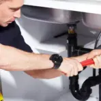 Man using wrench to tighten pipe under kitchen sink in well-lit space