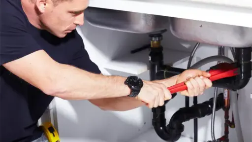 Man using wrench to tighten pipe under kitchen sink in well-lit space