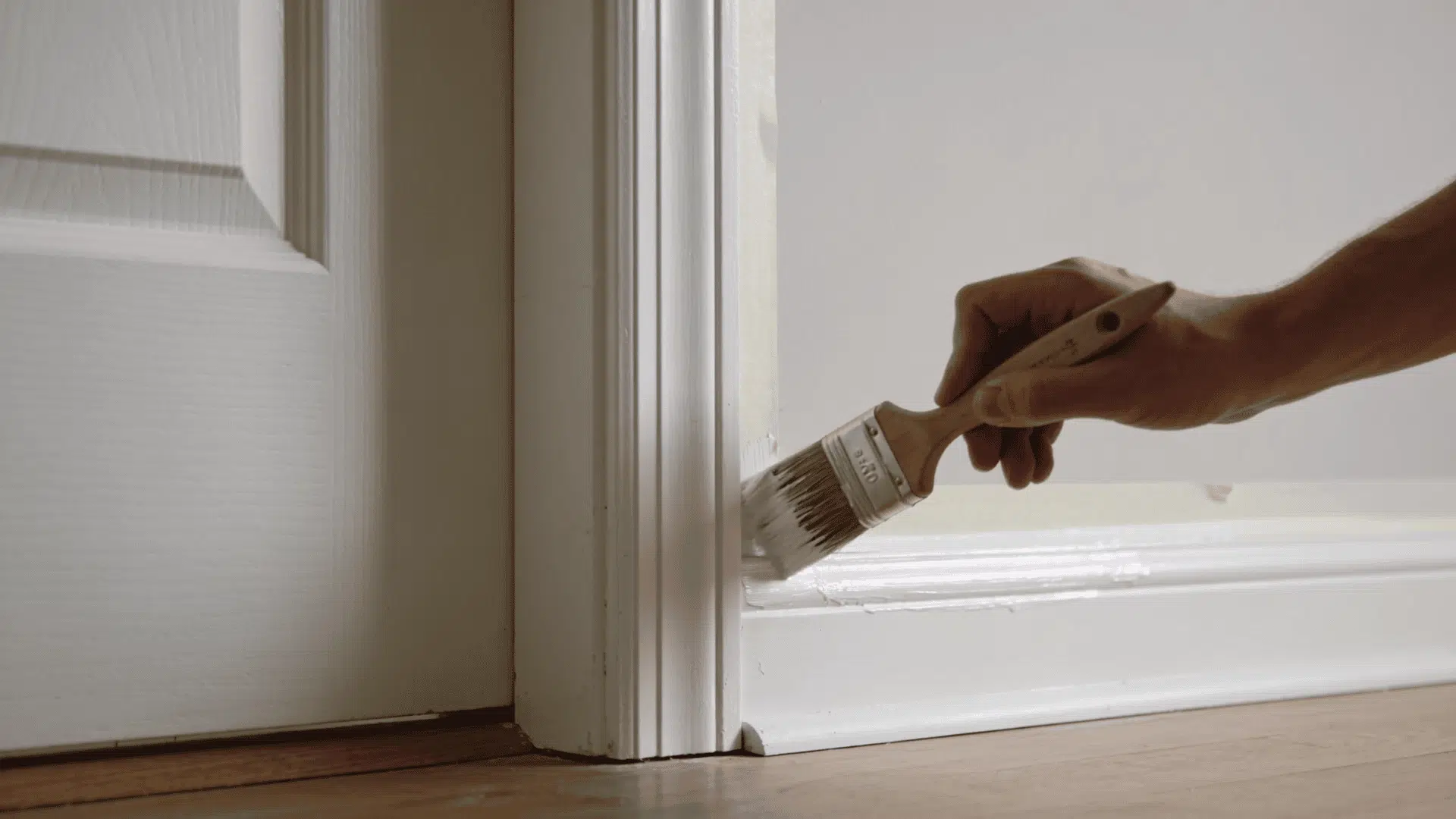 person carefully painting door trim and baseboard with angled brush and painter tape for clean edges