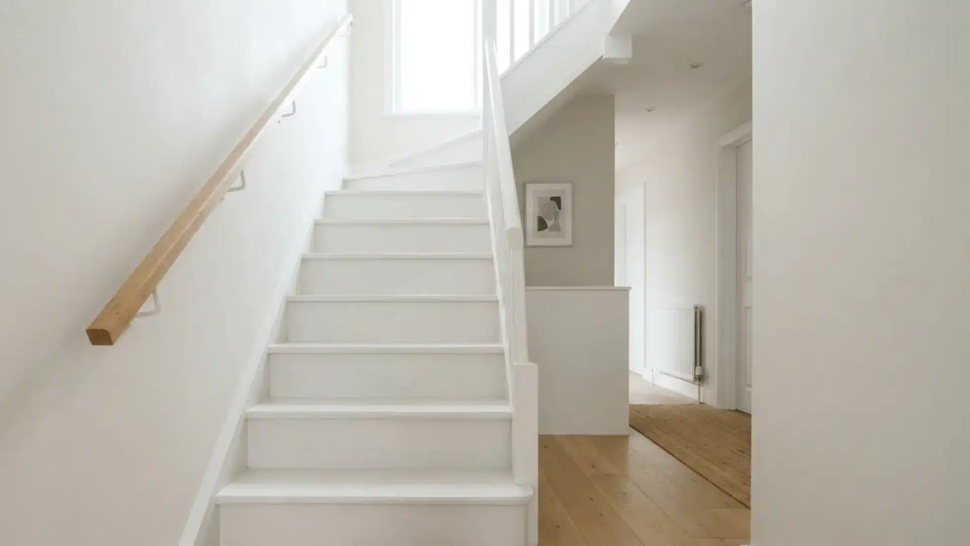 fully white painted stairs in a small bright stairwell with pale walls and simple railing