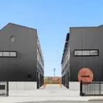 Two modern black buildings with metal siding and gated entry under clear sky
