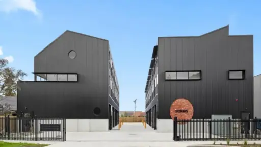 Two modern black buildings with metal siding and gated entry under clear sky