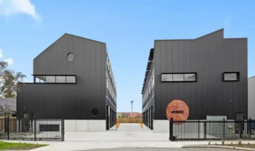 Two modern black buildings with metal siding and gated entry under clear sky