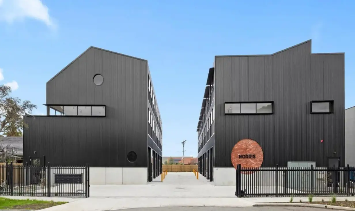 Two modern black buildings with metal siding and gated entry under clear sky