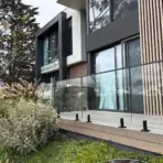 Modern house exterior with glass balcony overlooking lush garden and tall trees