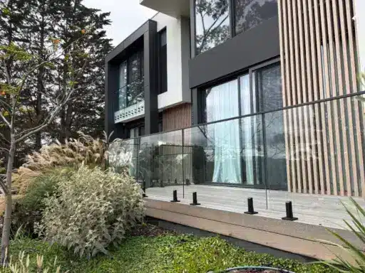 Modern house exterior with glass balcony overlooking lush garden and tall trees