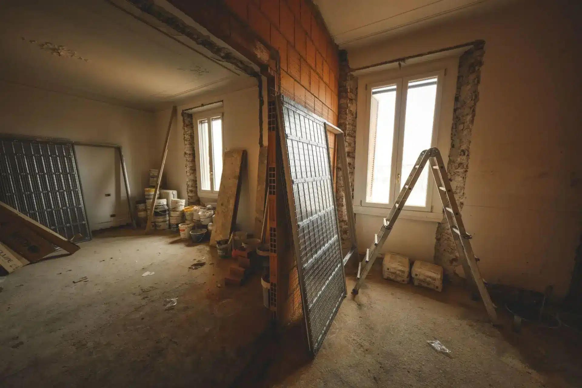 Renovation scene with ladder and construction materials in partially finished room with exposed brick walls