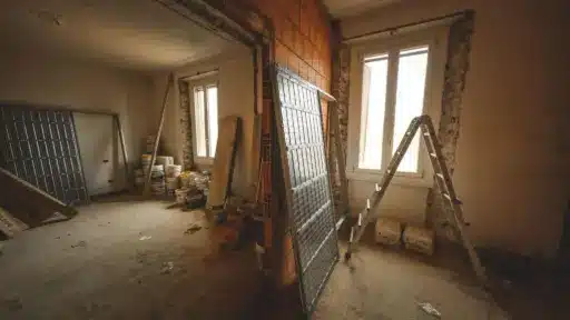 Renovation scene with ladder and construction materials in partially finished room with exposed brick walls