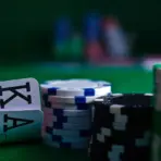 Poker chips and playing cards on green felt table in dimly lit casino setting