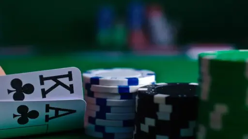 Poker chips and playing cards on green felt table in dimly lit casino setting