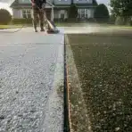 Worker pressure washing a driveway in front of a suburban house at sunrise