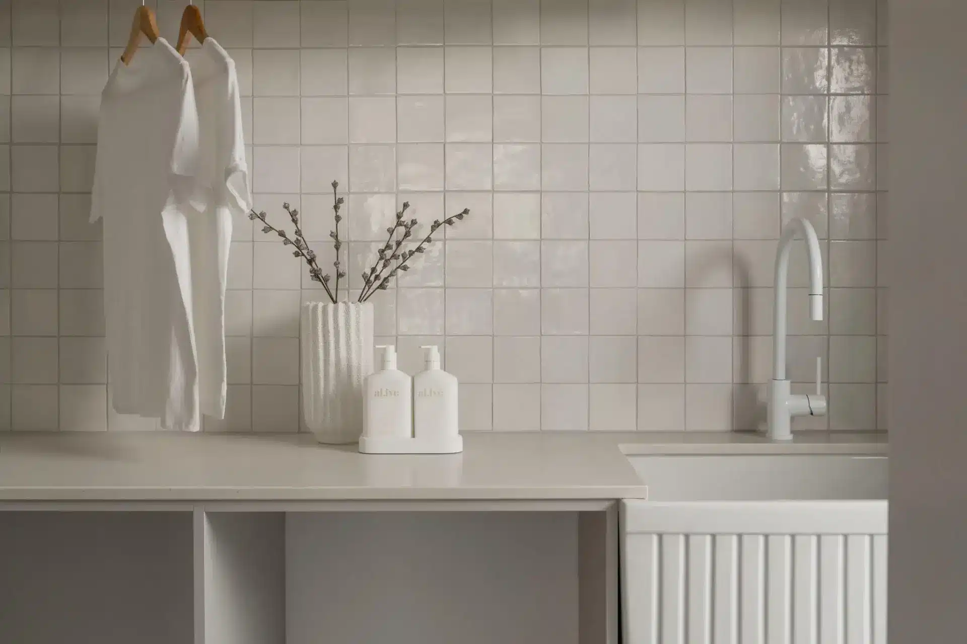 White t-shirts hanging in modern laundry room with tiled backsplash and countertop accessories