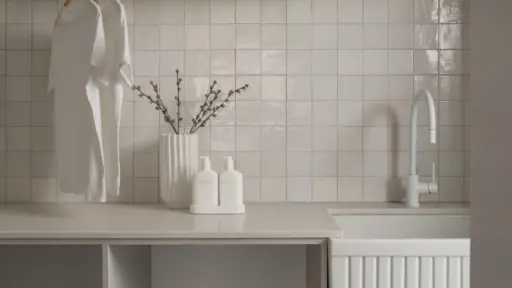 White t-shirts hanging in modern laundry room with tiled backsplash and countertop accessories