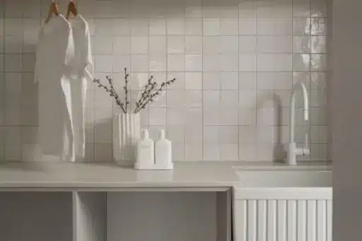 White t-shirts hanging in modern laundry room with tiled backsplash and countertop accessories