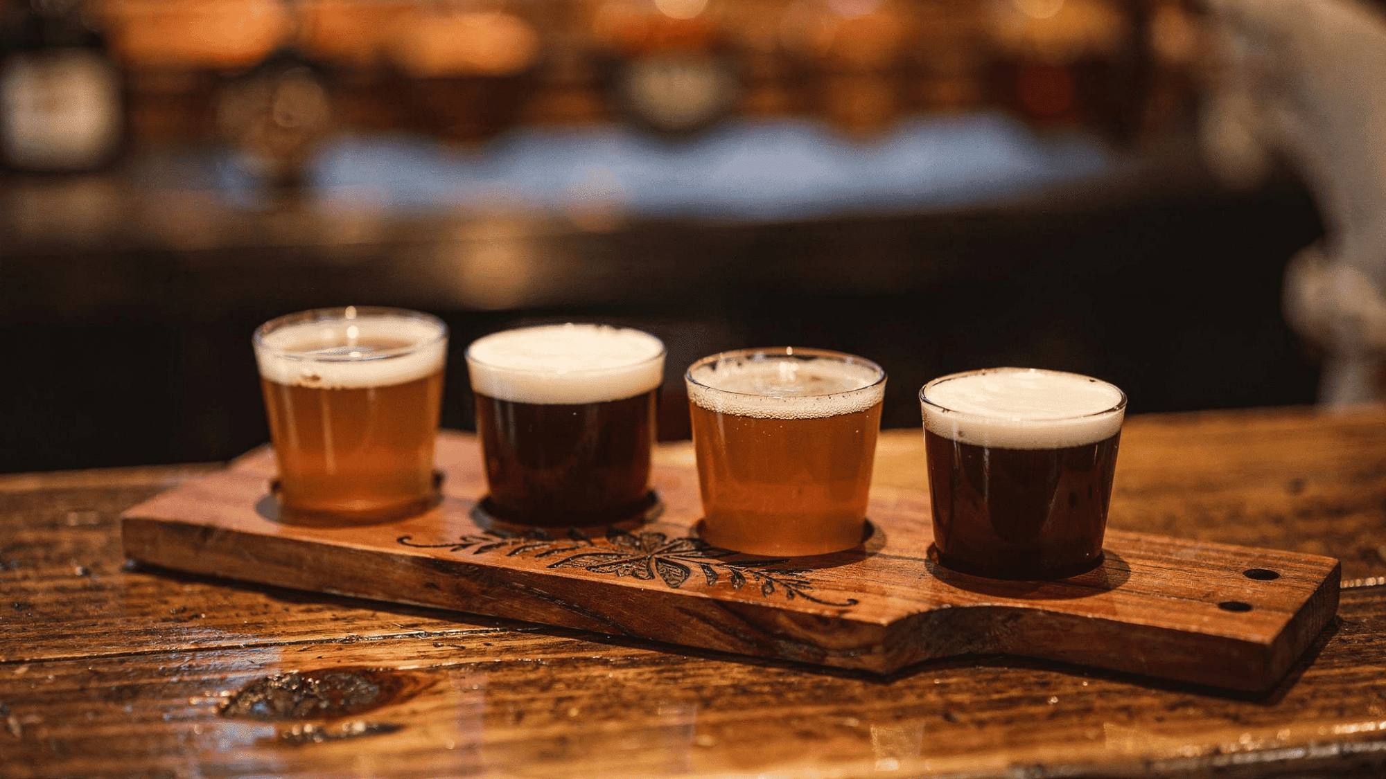wooden beer flight paddle with four amber beer glasses on a wooden bar