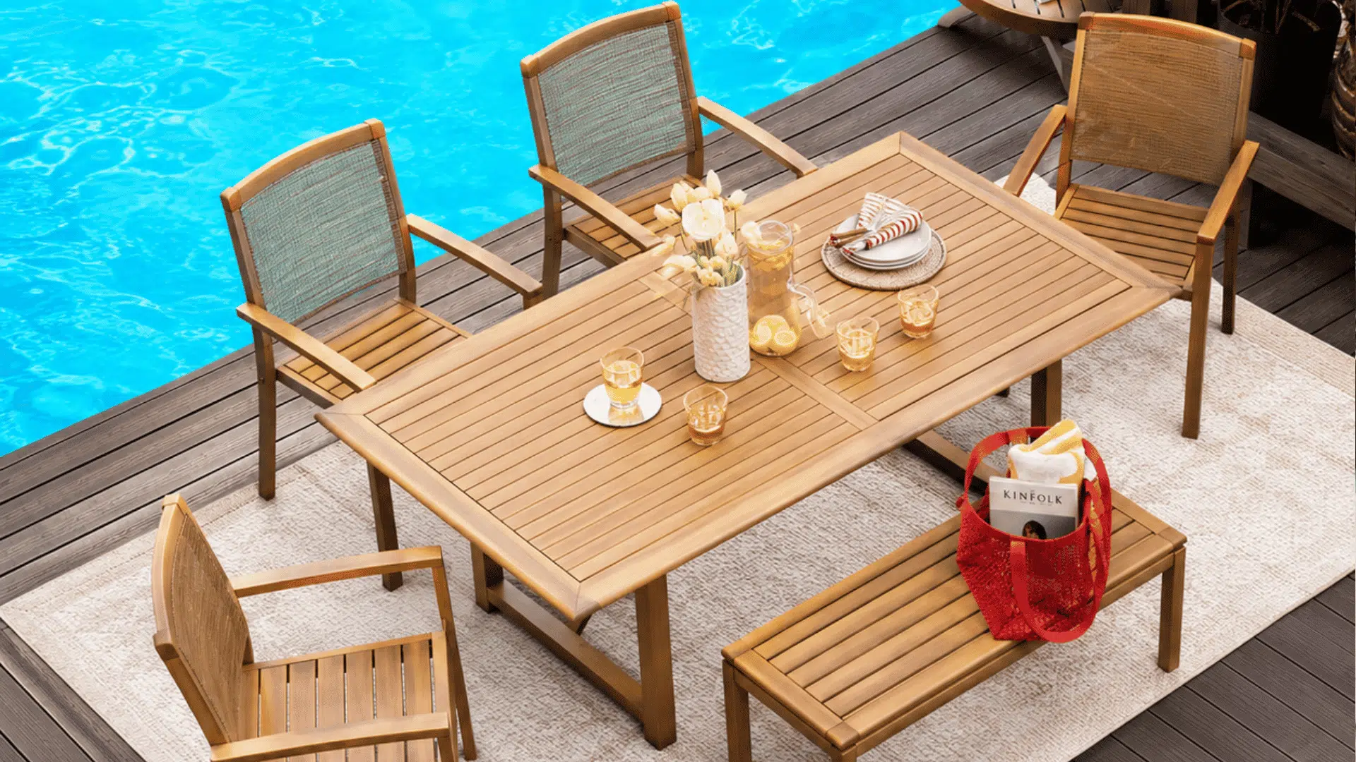 wooden outdoor dining table with matching chairs and bench placed on rug beside bright blue pool