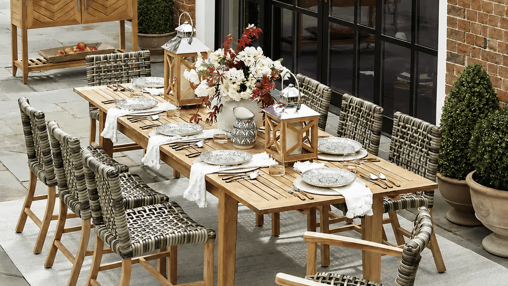 wooden outdoor dining table with woven chairs and floral centerpiece arranged on elegant stone patio