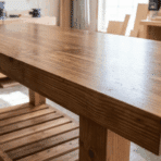 wooden workbench with smooth polished tabletop and lower slatted shelf standing in a bright woodworking shop