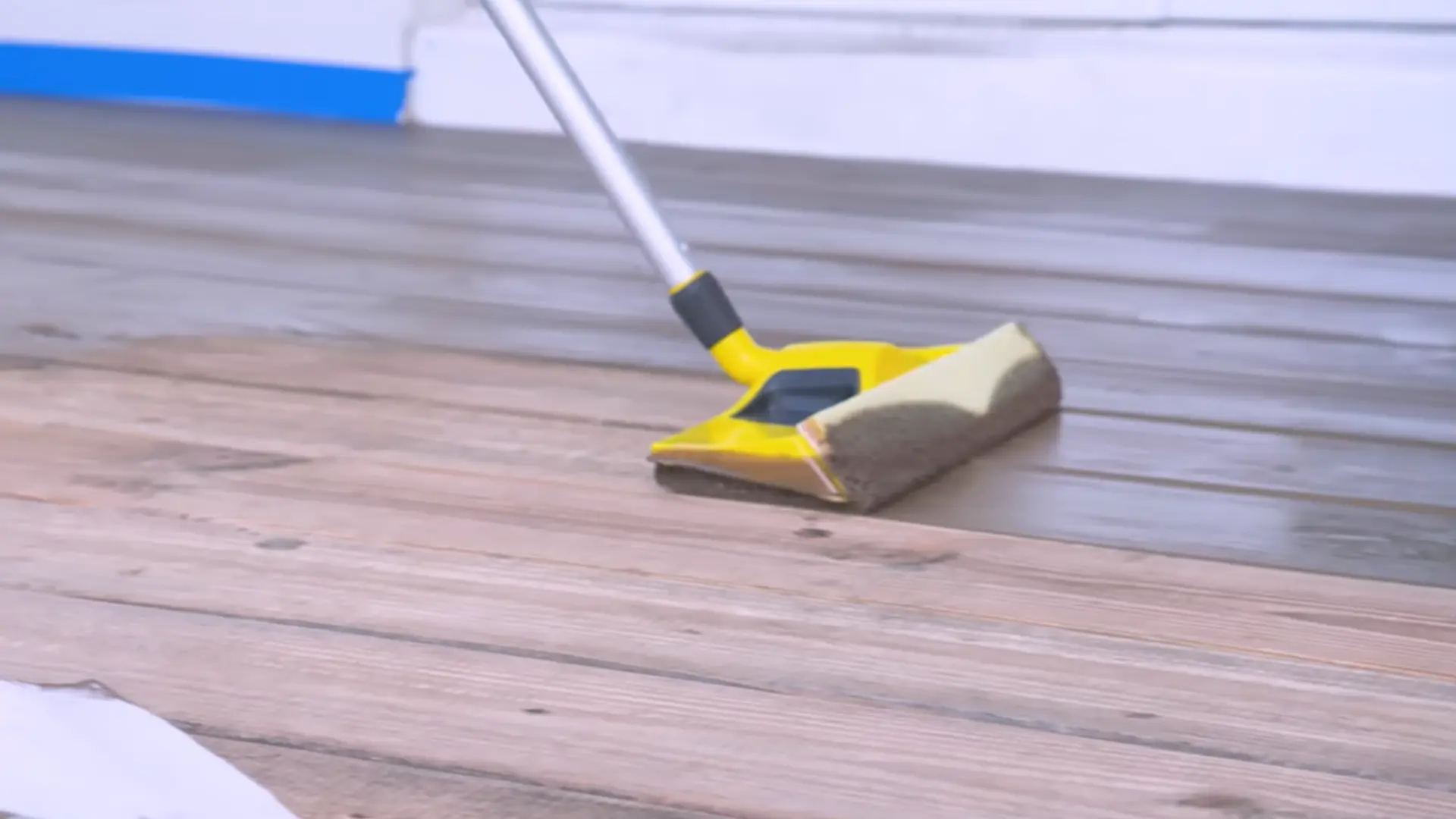 Yellow stain applicator spreading a dark finish across wooden deck boards
