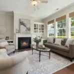 Cozy living room with fireplace, beige sofas, glass coffee table, and large windows with natural light