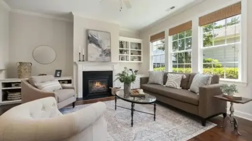 Cozy living room with fireplace, beige sofas, glass coffee table, and large windows with natural light