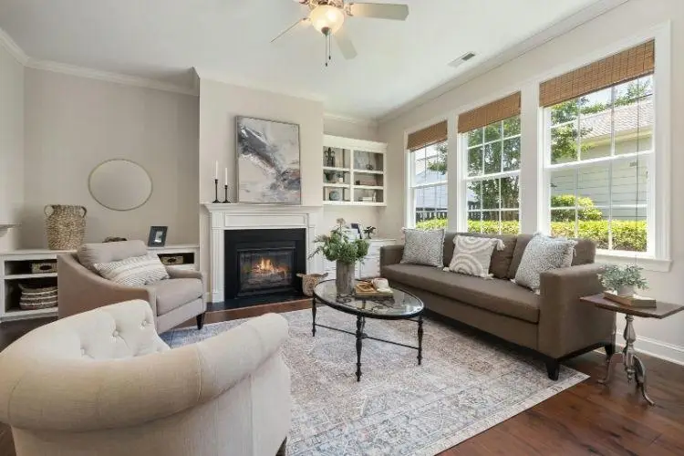 Cozy living room with fireplace, beige sofas, glass coffee table, and large windows with natural light
