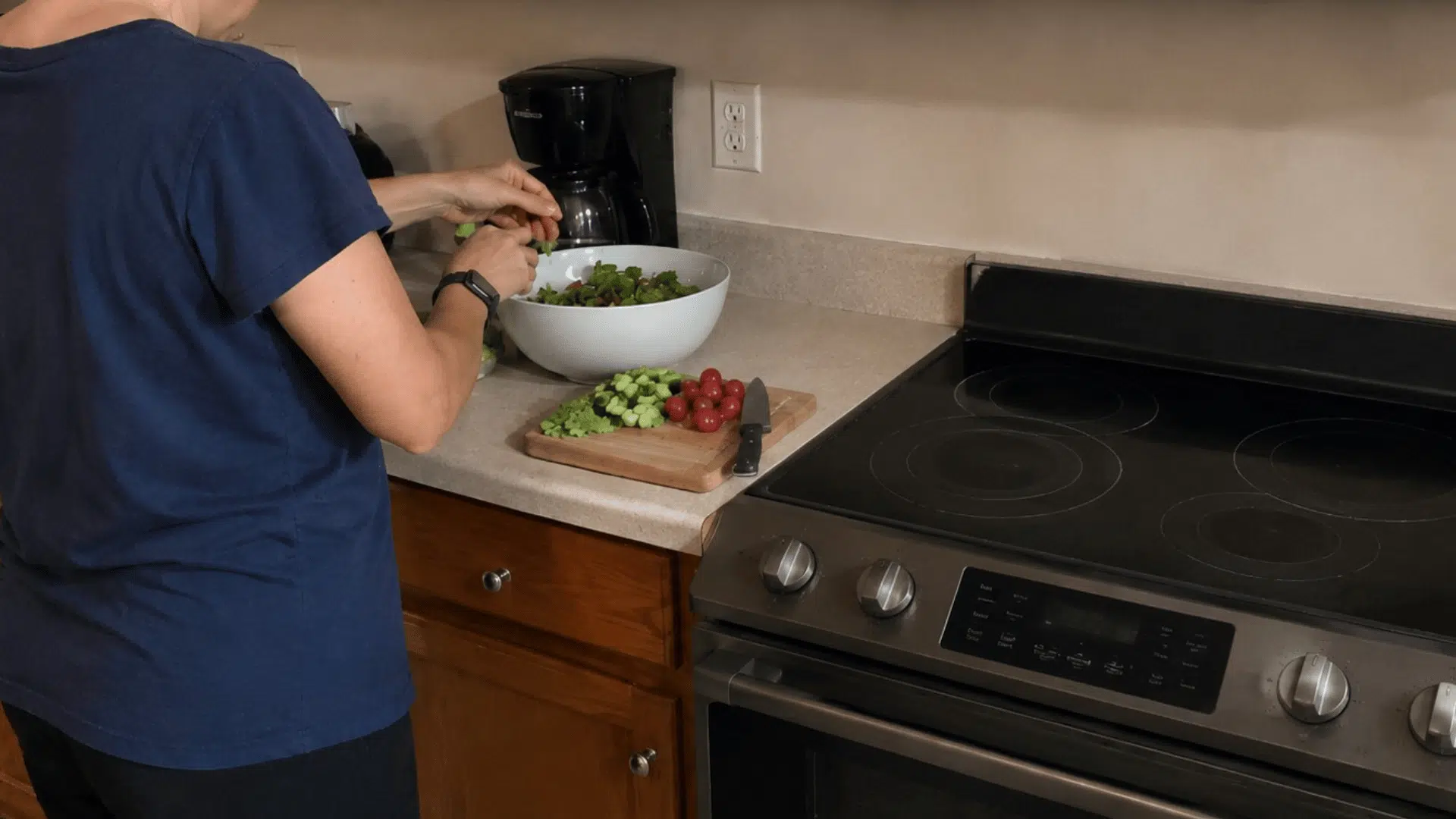 person preparing a fresh salad beside an unused stove to avoid adding extra heat to the kitchen